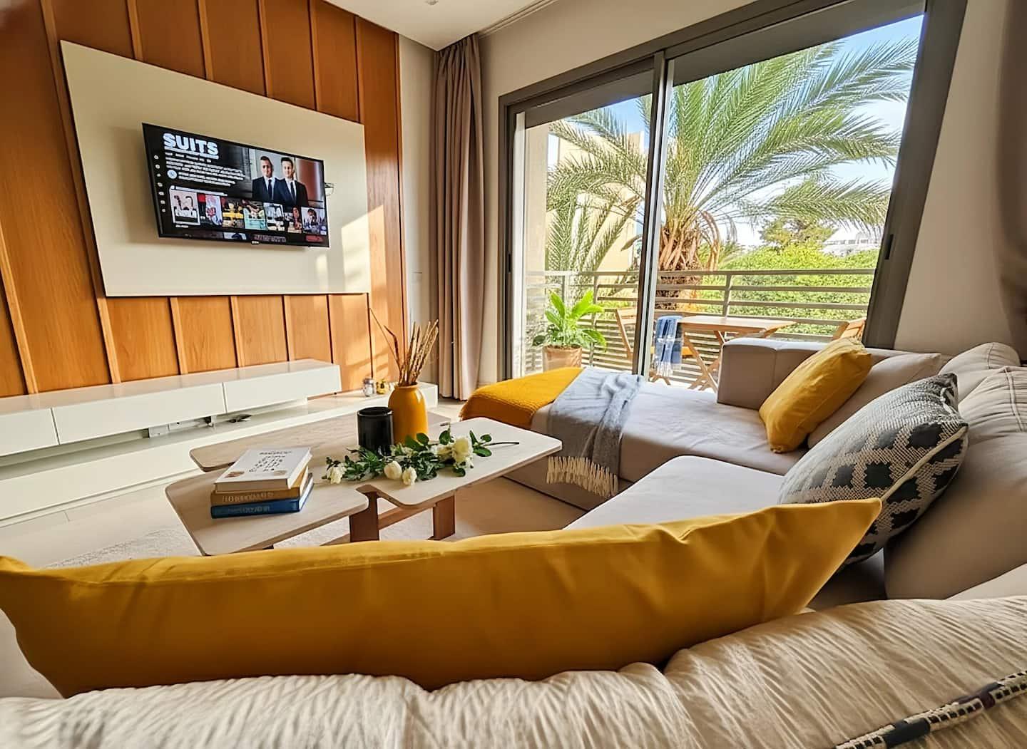 Salon cosy jaune ouvert sur un palmier — Maya Suites Casablanca
